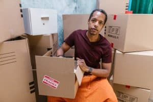 A man sitting among packed moving boxes, preparing for relocation. Caption: Hiring movers early can help you avoid last-minute stress and ensure a smooth transition. 